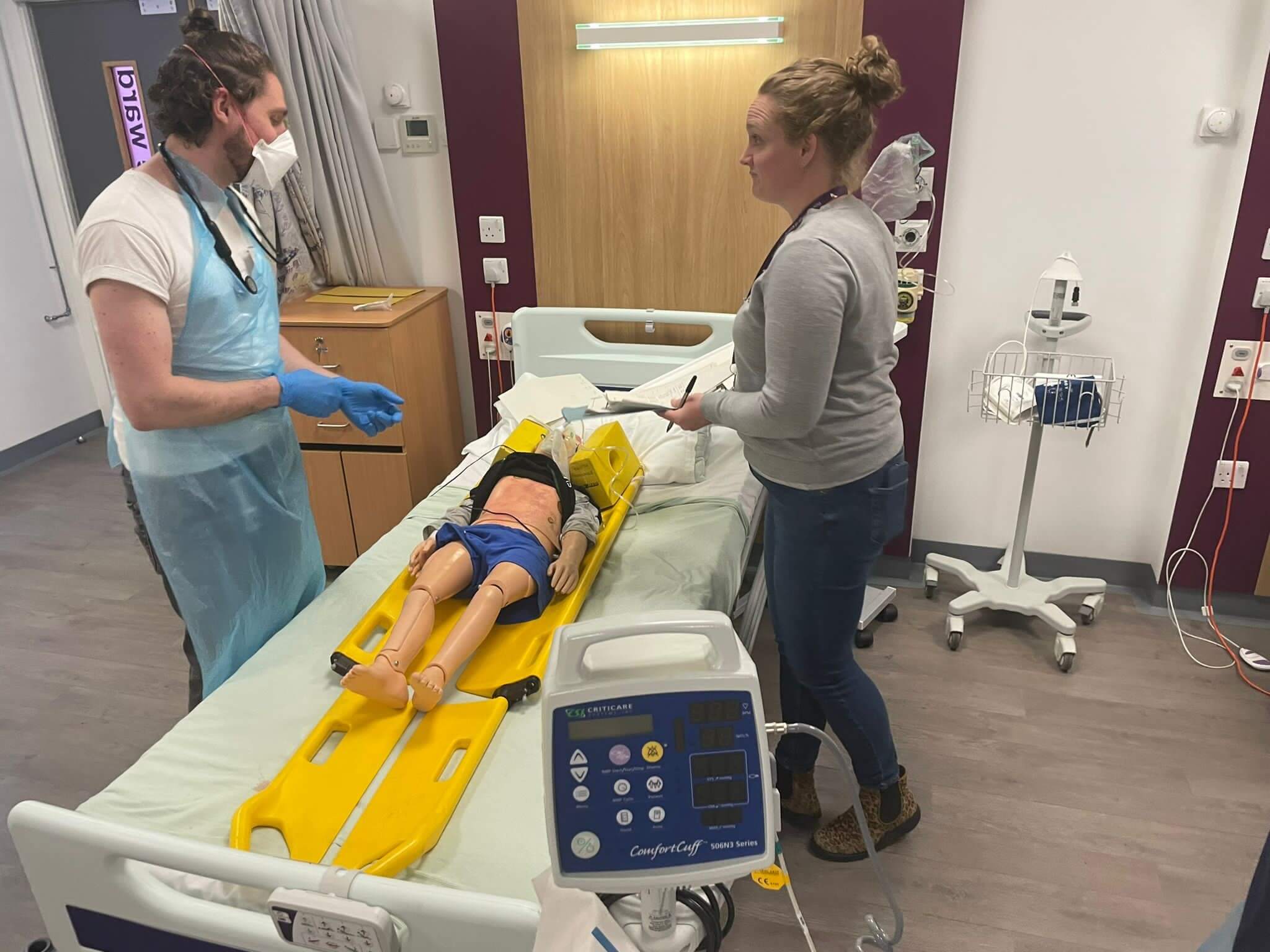 Two NHS staff look at and discuss a medical mannequin