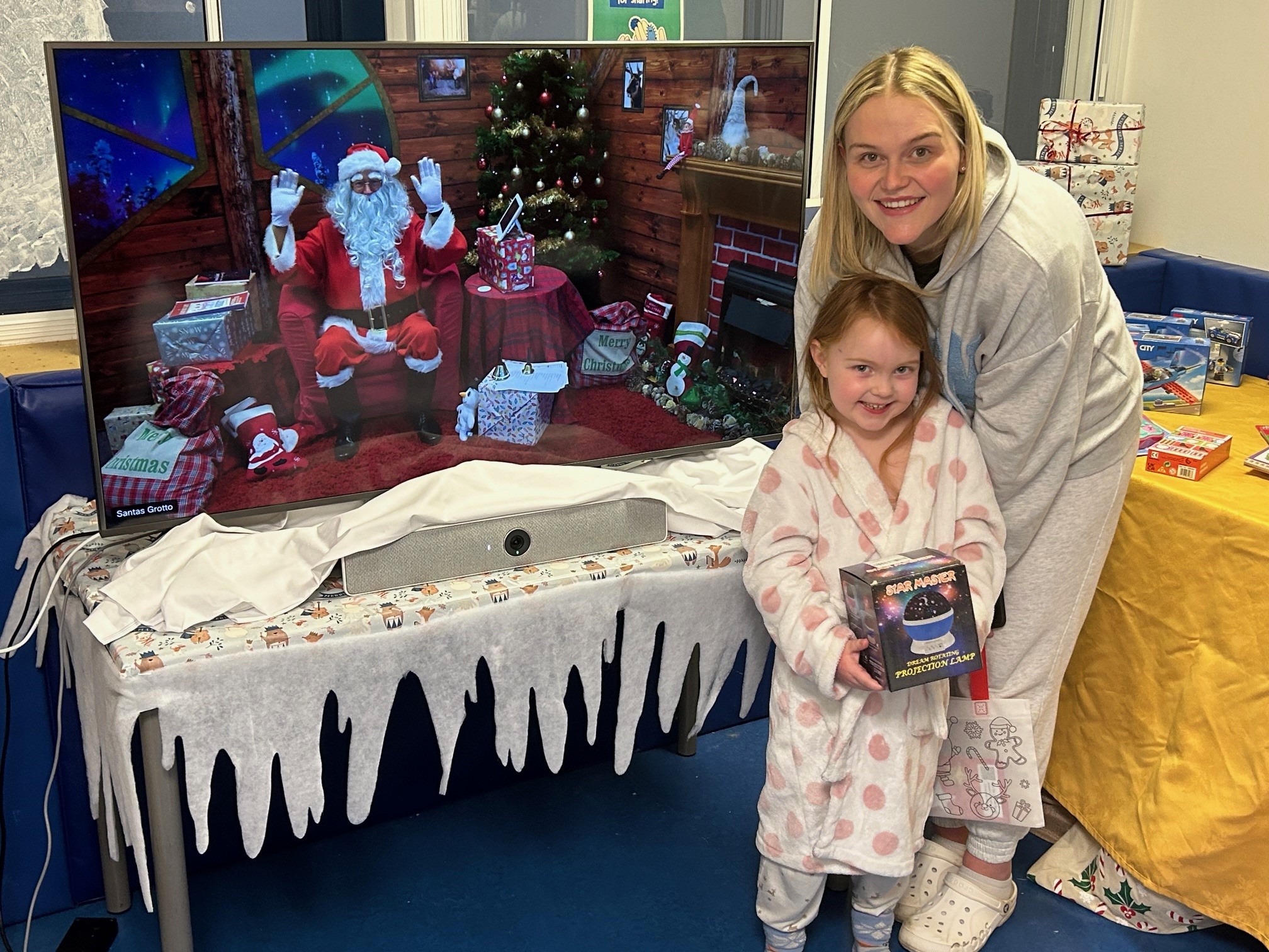 Photo of a mother and her young daughter standing next to a TV which shows Santa Claus on a remote video connection