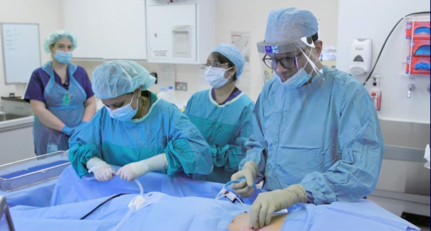 Prof Munavvar, surrounded by a few other medical staff, all wearing medical clothing, performing a medical procedure on a patient