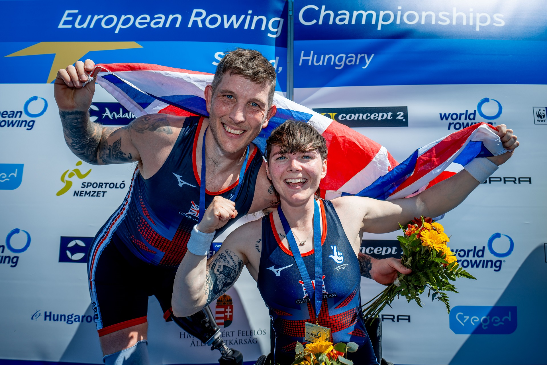 Photo of Gregg Stevenson and Lauren Rowles wearing medals, holding the British flag as they celebrate their achievement