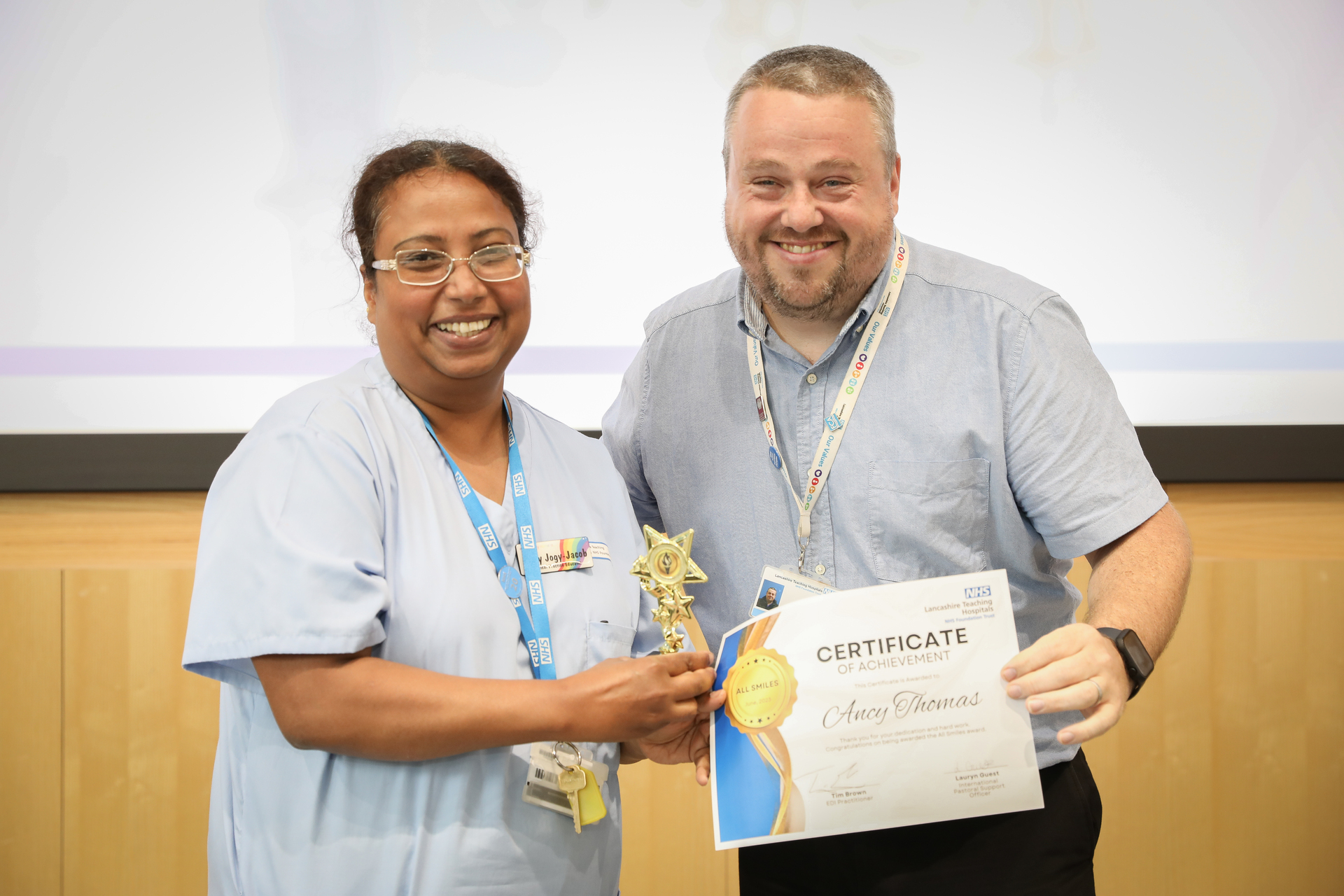 Staff member holding award certificate, smiling next to another person