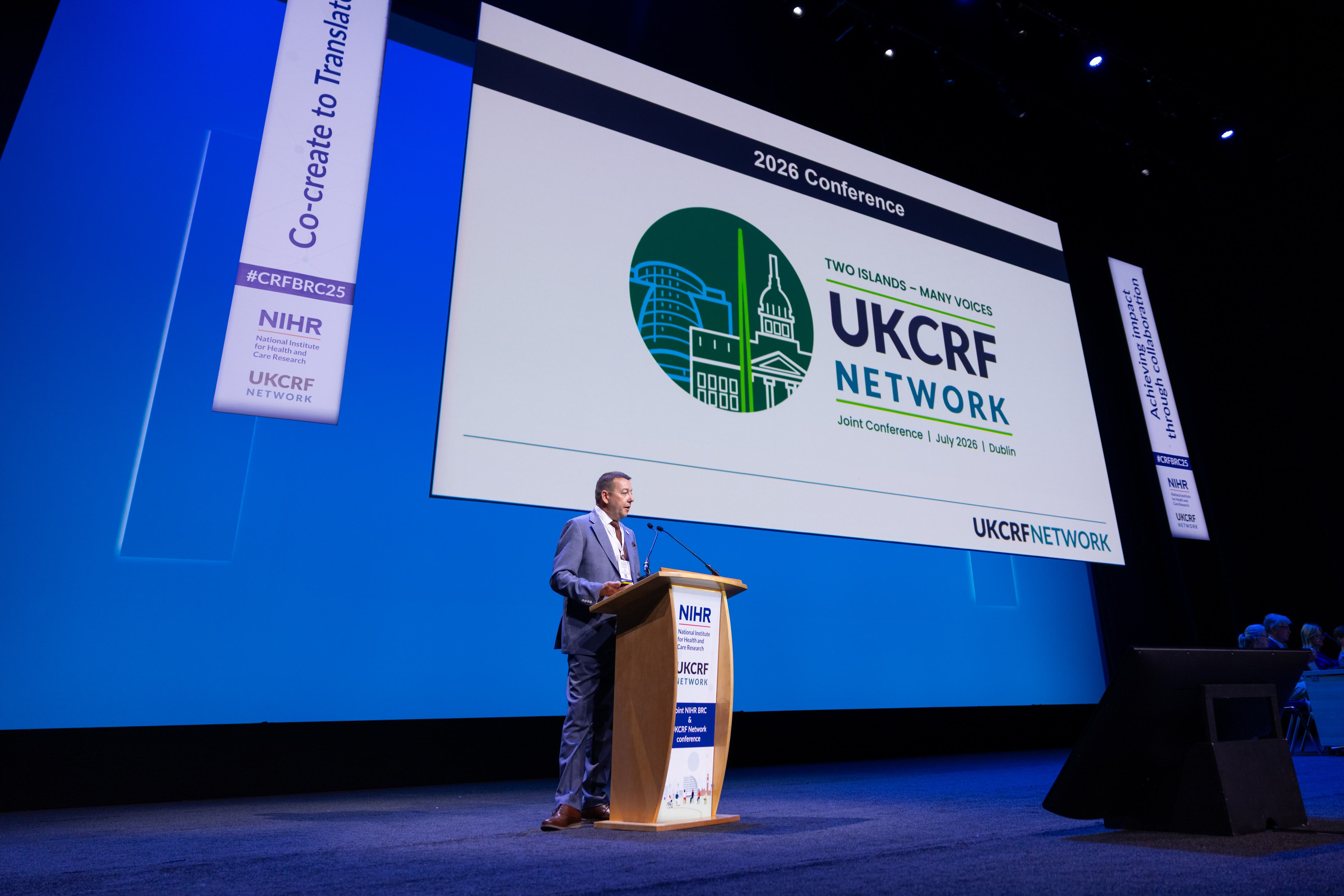 A man speaking at a podium with a giant digital screen behind him