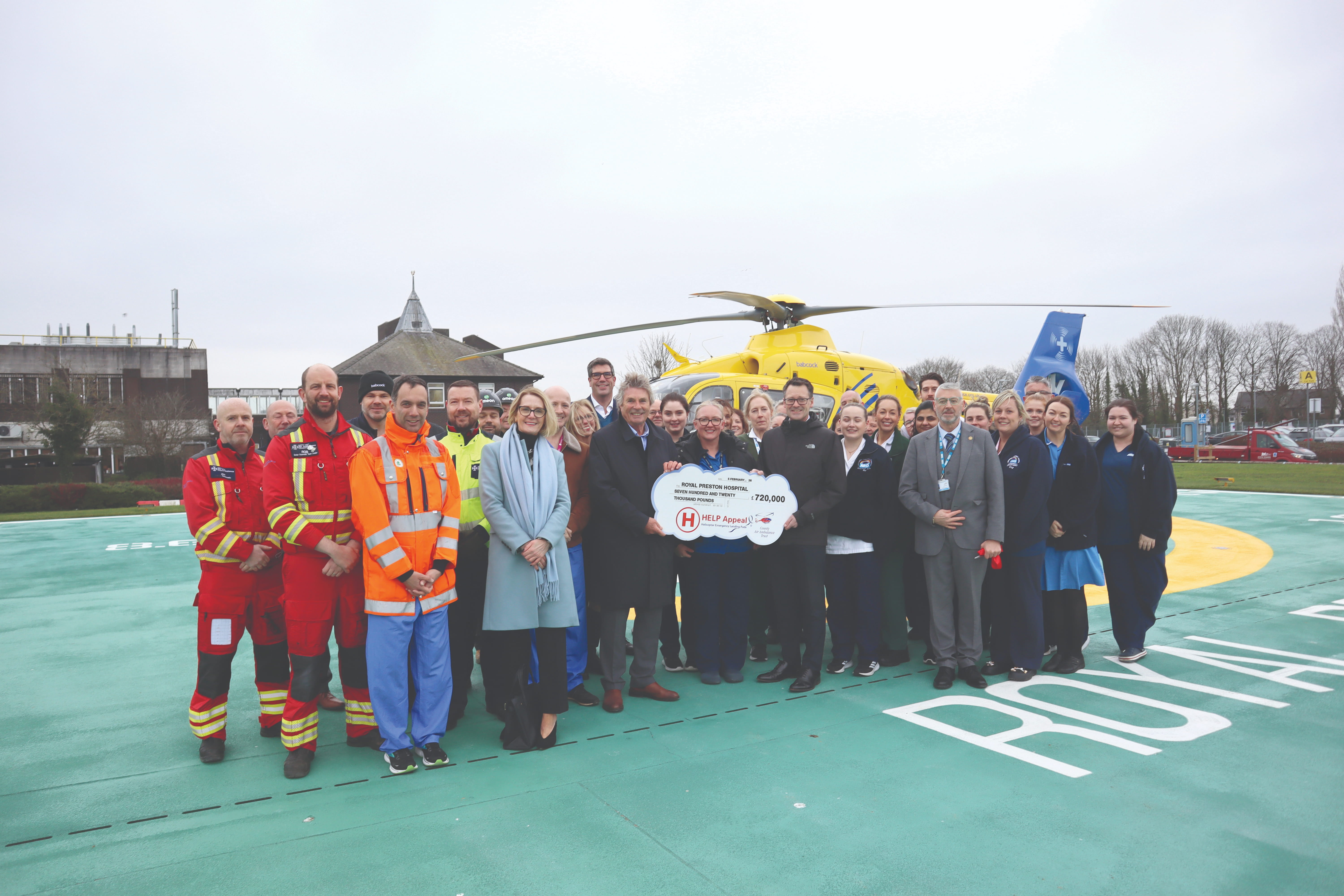 Helipad and staff standing together, smiling, holding a sign