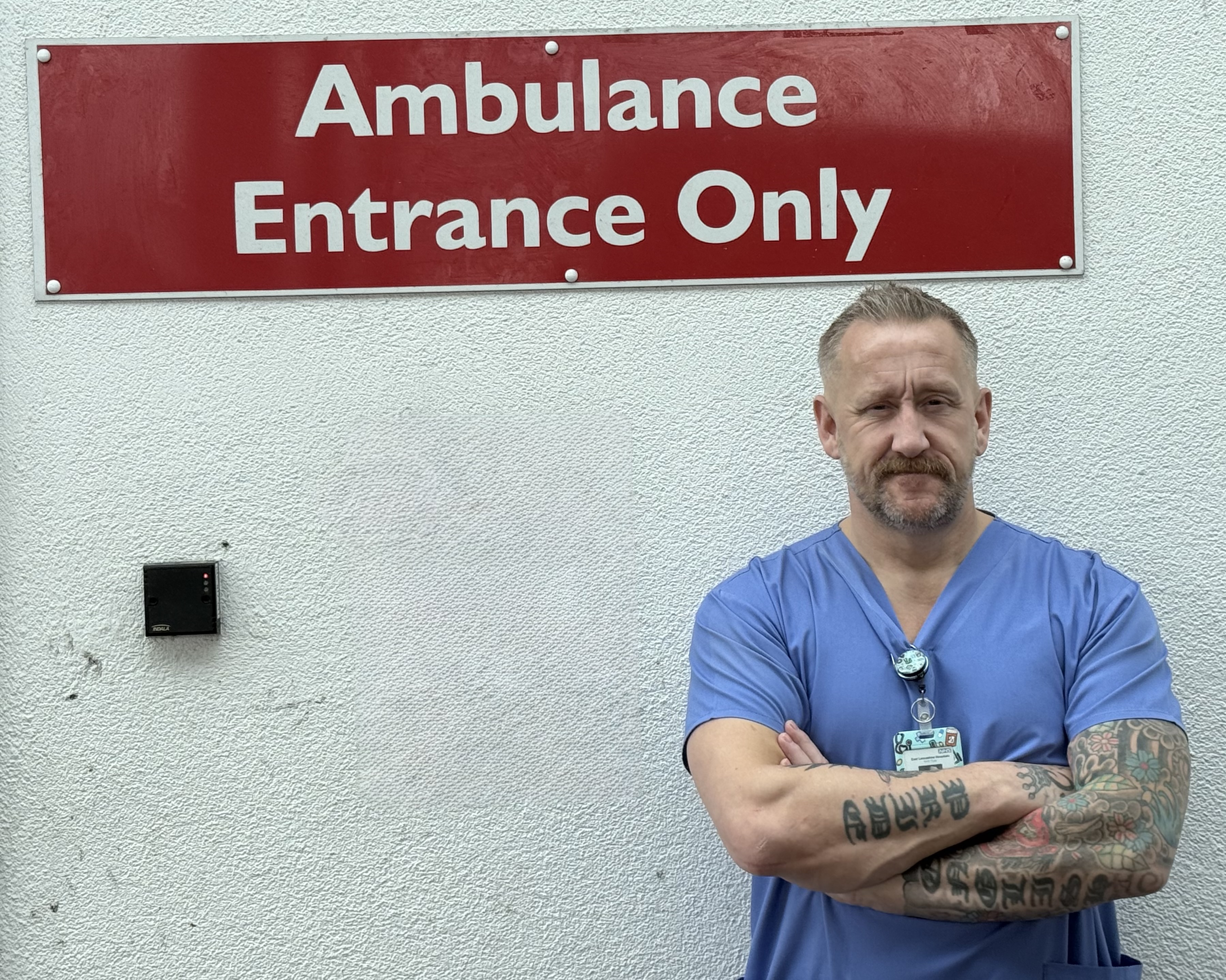 Paul Tinstill wearing medical clothes, standing with an Ambulance Entrance Only sign behind him