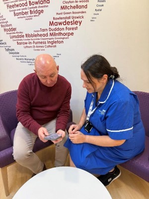 A photo depicting a uniformed NHS employee showing a pamphlet to a patient