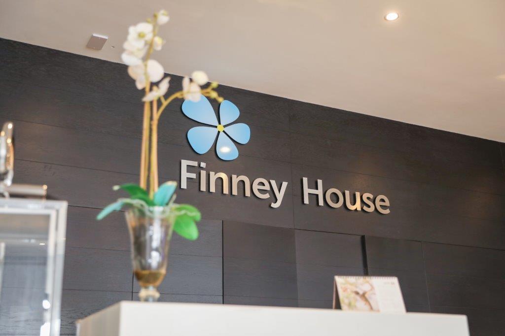 A photograph of the Finney House reception, taken from a lower angle showing a vase of flowers, and a Finney House logo and reception desk on the background