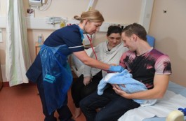Photo of staff member using a stethoscope on a baby while two parents hold it